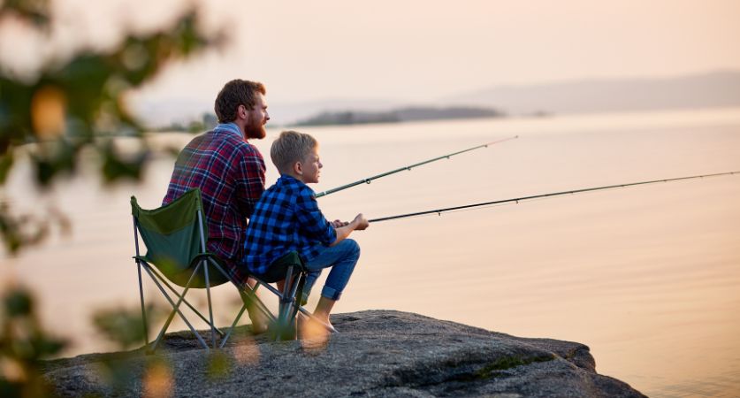 Father and son fishing from a rock at a lake at sunset