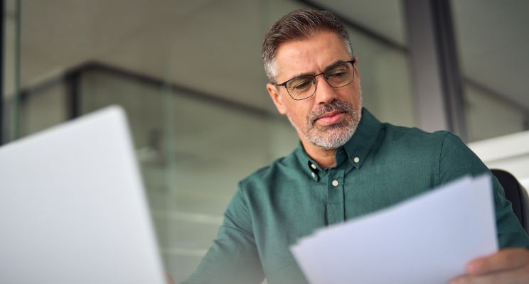Man in glasses reviewing papers at a laptop