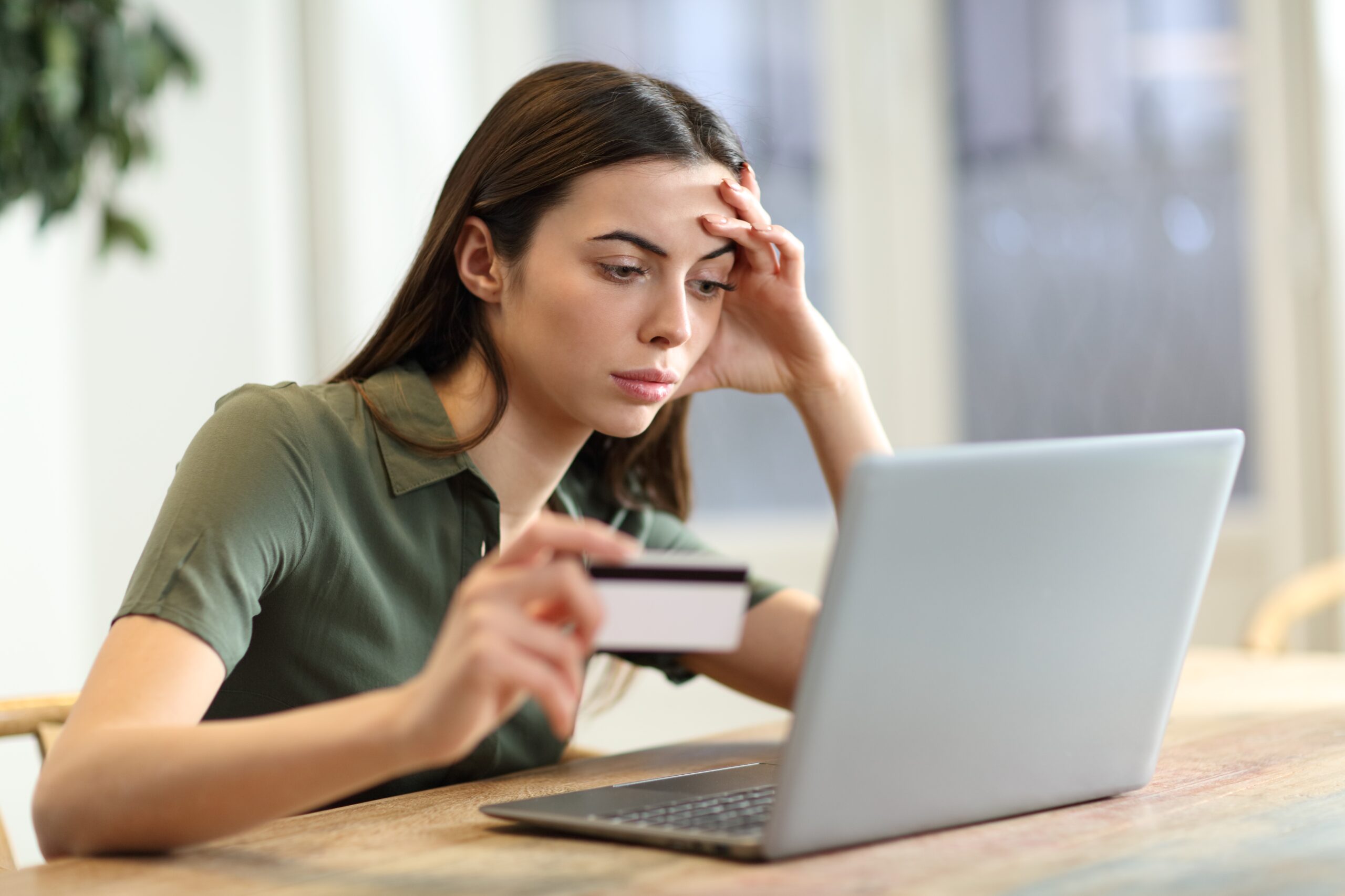 Stressed young woman holding a credit card at her laptop