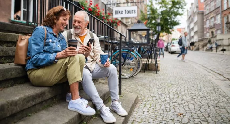 Older couple with coffee sitting on steps of a cobblestone street