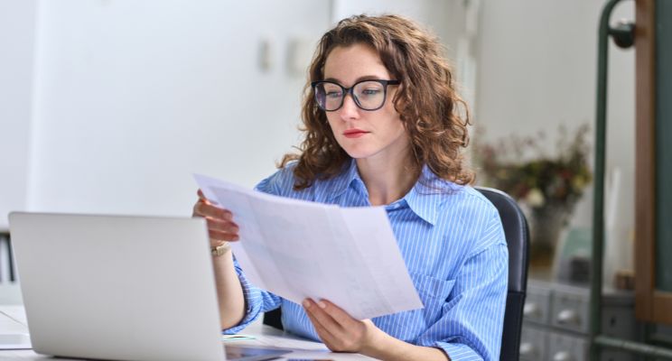 Woman in glasses reading a document beside her laptop