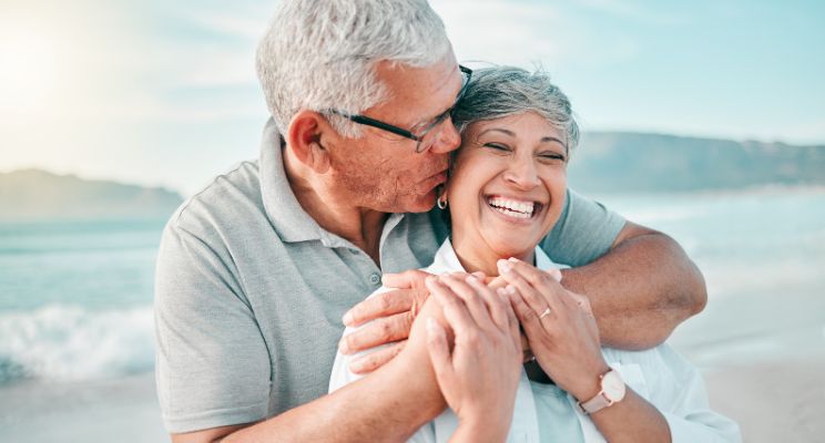 Retired man hugging his wife from behind on a beach