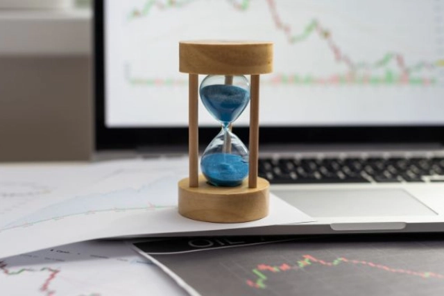 Hourglass on stock market charts in front of a laptop