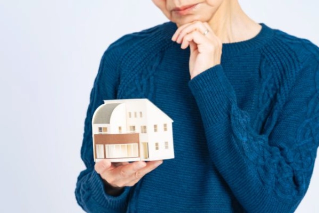 Woman holding a small model house, thinking