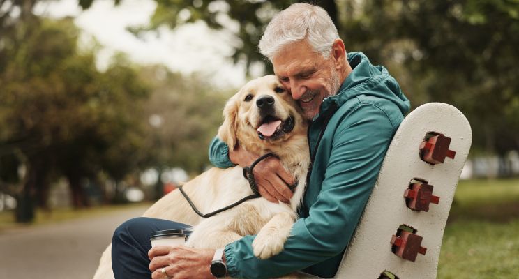 Smiling older man hugging his golden retriever on a park bench