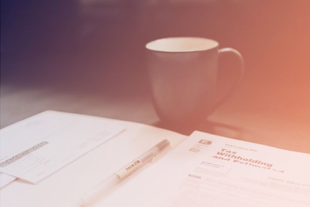 Tax withholding forms and a pen on a desk beside a coffee mug