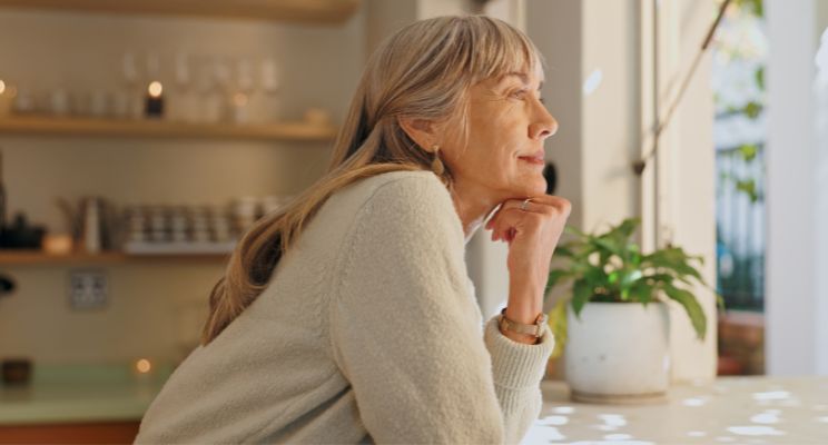 Retired woman resting her chin on her hand, looking out a window