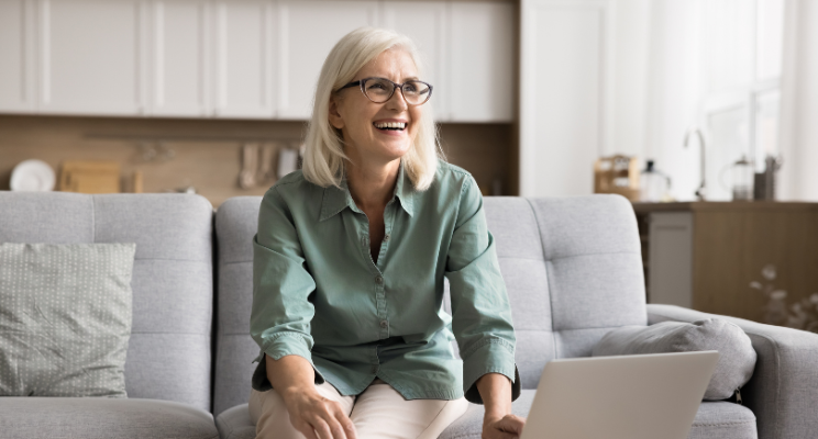 Smiling older woman on a sofa with a laptop beside her